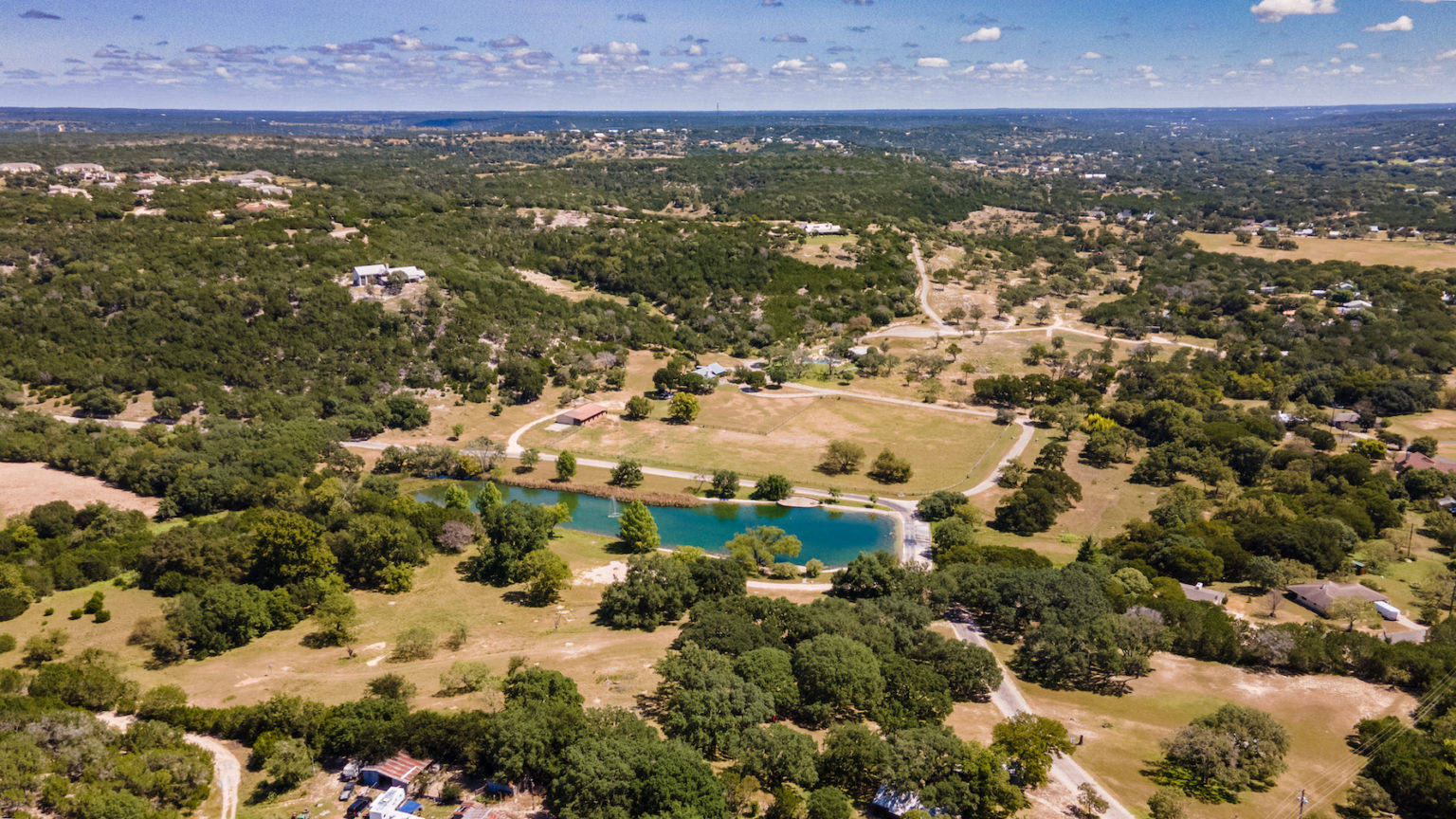 Aerial view of oak-dotted Hill Country land stretching to the horizon, with a small pond