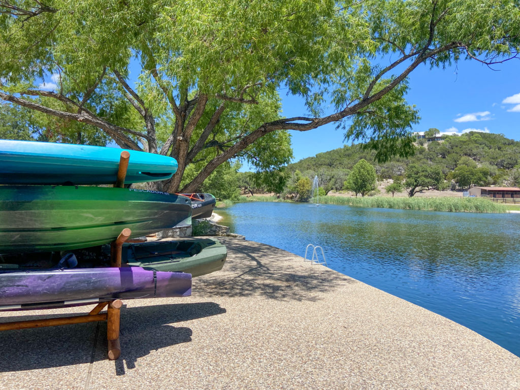 Colorful kayaks stacked on a rack beside a calm lake with tree-covered hills in the distance