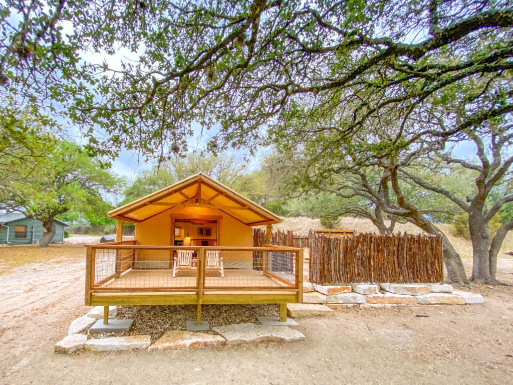 Glamping tent with a wooden deck beneath large oak trees