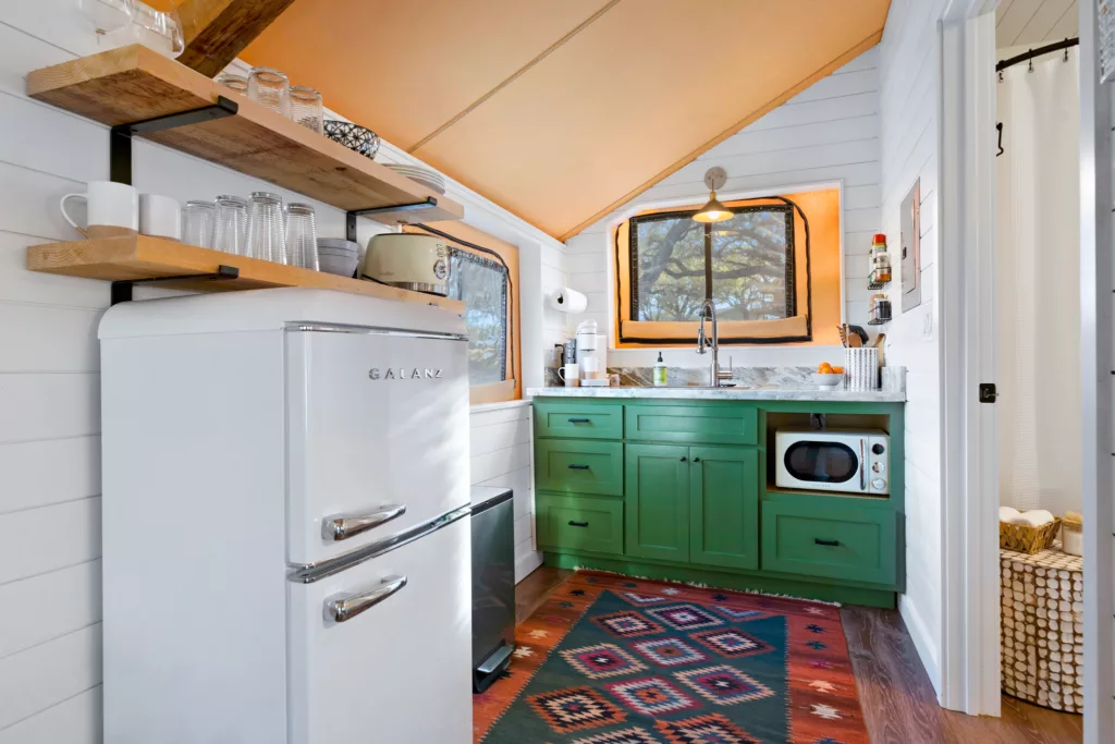 Kitchenette with a white refrigerator, green cabinets, a microwave and open shelves with glasses