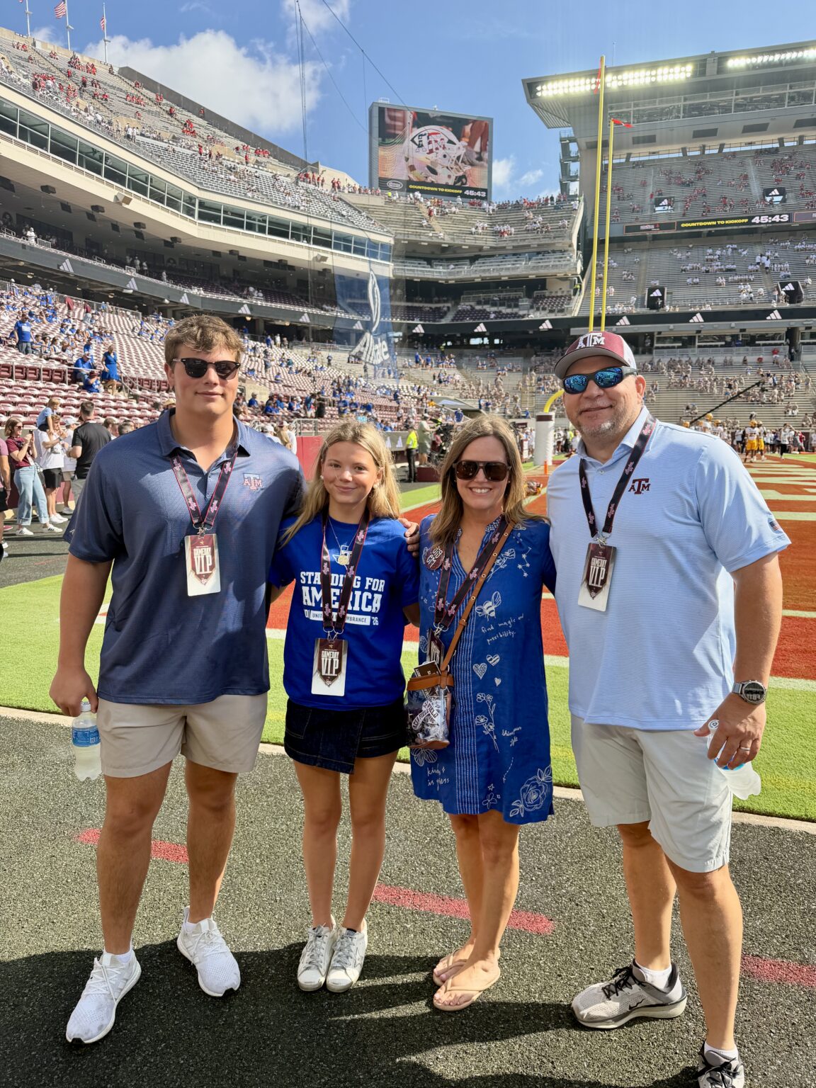 Jeremy and Kelly with their children, Jackson and Annie, smiling together on the sidelines of a college football stadium